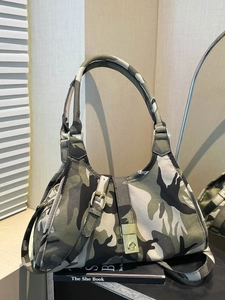 Vintage camouflage canvas shoulder bag with gold buckles on a book in a chic room