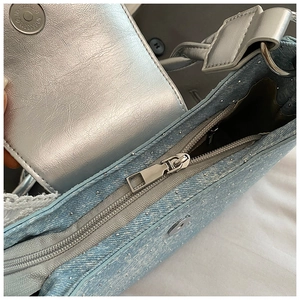 Détail du sac en denim bleu clair avec boucle en métal argenté et fermeture aimantée