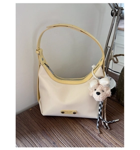 Détail d'un sac à main beige en cuir souple avec plaque logo et pendentif chien en peluche