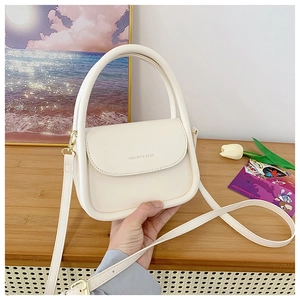 Detail of cream white leather mini handbag with circular handle and gold metal hooks
