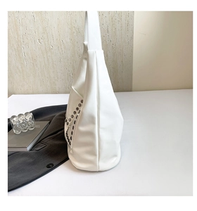Detail of white tote bag featuring decorative silver rivets on side pocket texture