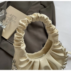 Detail shot of pleated cream cloud bag with elegant pearl chain and soft texture