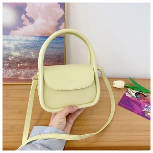 Detail of light yellow mini handbag with curved handle and thin shoulder strap on wood
