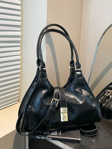 Vintage minimalist black glossy shoulder bag with gold buckle on artistic book display