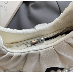 Detail of cream pleated cloud bag with silver zipper and decorative pearl chain