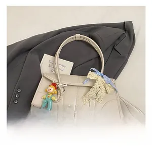 Detail of cream leather tote bag with blue plaid bow and cute cartoon pendant charm