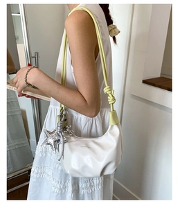 Close-up of white croissant bag featuring yellow knotted rope strap and star charm