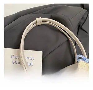 Detail of beige tote bag handle with double stitching and blue plaid bow accessory