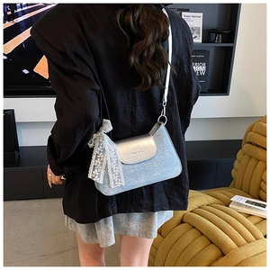 Détail du sac en jean bleu avec rabat argenté et nœud décoratif en dentelle blanche