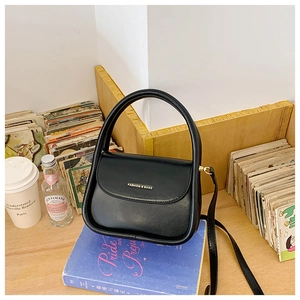 Detail of black faux leather crossbody bag on vintage book with gold FASHION logo
