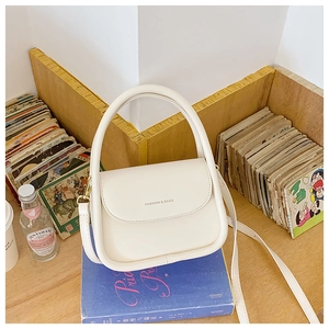 White mini crossbody bag with Fashion & Bags text on blue books in vintage setting