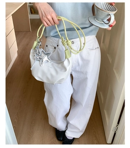 Close-up of a white crescent shoulder bag featuring a silver star charm and thin cord strap