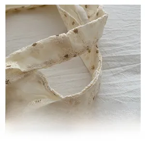 Detail showing white lace handle with delicate daisy embroidery on canvas tote bag
