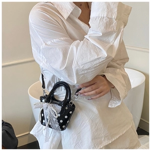 Close-up of mini polka dot handbag with white lace bow and pearl charm worn by model