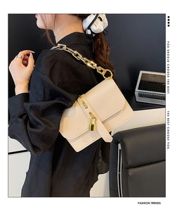 Detail of beige flap shoulder bag with gold chain strap and padlock charm on model