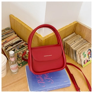 Detail of red small square crossbody bag on a book with golden hardware and hand strap