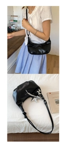 Detail of black croissant crescent bag with glossy texture and silver charms