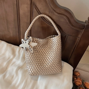 Detail of champagne gold woven tote bag featuring beige double star charms and sleek finish