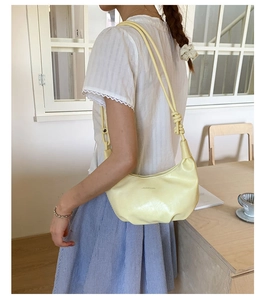 Detail of light yellow crescent bag with stylish knot strap and smooth leather texture