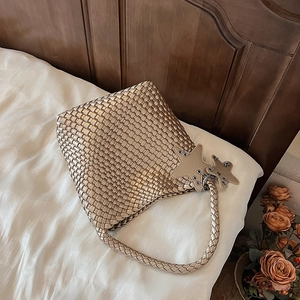 Detail of champagne gold woven tote bag with star charms on white silk fabric