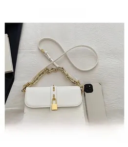White leather shoulder bag with gold padlock clasp and chain strap next to a phone
