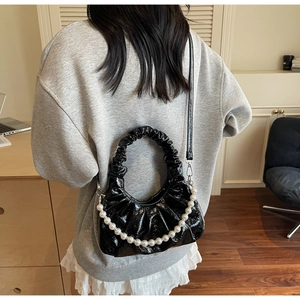 Close-up of black glossy pleated cloud bag with elegant white pearl chain and strap