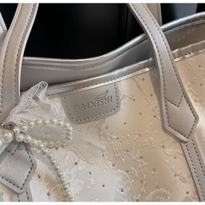 Dettaglio borsa shopper argento con ciondolo di perle, pizzo e strass brillanti sulla borsa