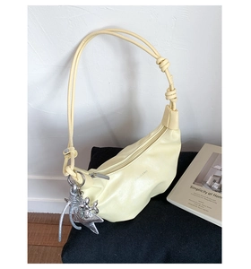 Close-up of pale yellow croissant bag with natural pleats and silver balloon dog charm