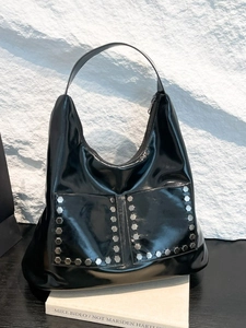 Fashionable black glossy tote bag with silver studs on a white textured background