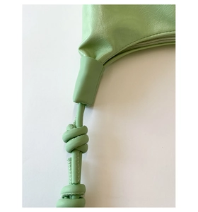 Macro detail of light green croissant bag with lychee texture and knotted strap design