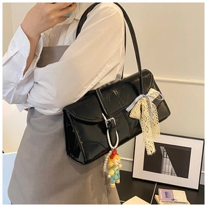 Detail of black patent leather tote bag with pearl doll pendant and lace bow accessory
