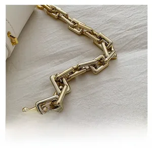 Detail shot of a glossy gold chain strap on a white leather baguette shoulder bag