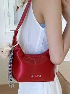 Sac hobo en cuir rouge avec logo argenté, porté épaule avec porte-clé ours et corde tressée