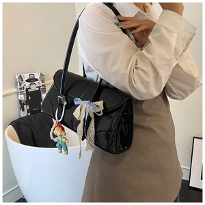 Detail of black patent leather tote bag with blue lace bow and pearl doll pendant