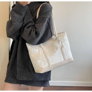 Dettaglio della borsa tote in pizzo beige con fiocco e ciondolo di perla sulla modella
