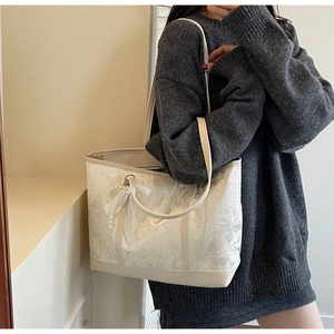 Dettaglio della borsa tote in pizzo crema con ricamo floreale e ciondolo a fiocco di perle