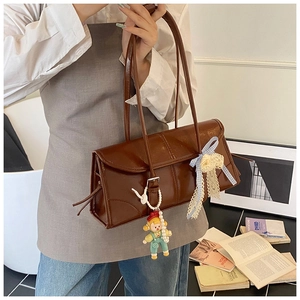Close-up of brown PU leather shoulder bag with a blue plaid bow and cute doll charm