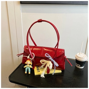 Detail of red patent leather tote with doll charm, lace bow and long shoulder straps