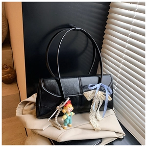Detail of black tote bag with pearl chain, doll pendant and lace bow on beige coat
