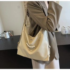 Detail of cream tote bag featuring elegant gold chain and pearl strap decoration