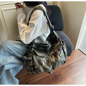 Detail of a large camouflage canvas shoulder bag showing front flap pockets and wide strap