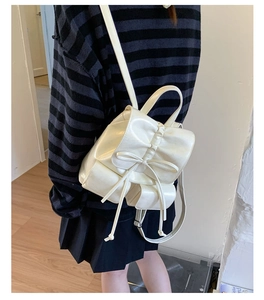 White glossy PU leather backpack with bow detail shown on a model in a minimal indoor setting