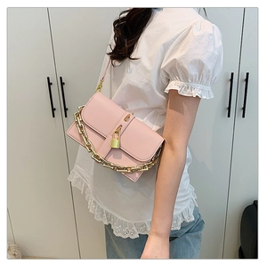 Close-up of light pink crossbody bag with bold gold chain strap and metal lock detail