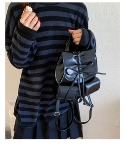 Detail of a shiny black bow backpack with drawstring and twin front pockets