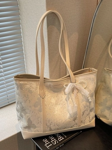 Borsa tote beige con stampa a farfalla e ciondolo di pizzo e perle in un ambiente interno