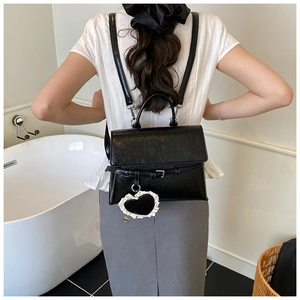 Model wearing black faux leather backpack with heart charm in a bright lifestyle setting