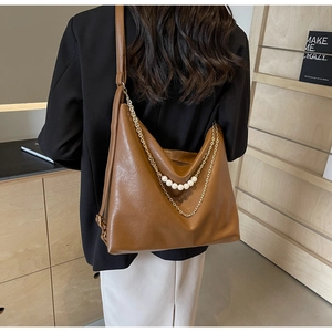Brown leather tote bag featuring elegant gold chains and pearl strap details on a model