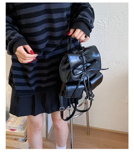 Detail of black glossy faux leather backpack featuring a bow design and drawstring closure