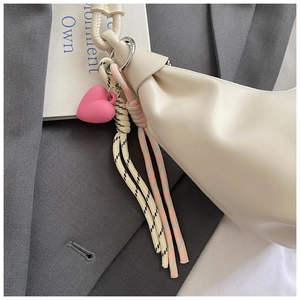 Detail of off-white leather dumpling bag featuring pink heart charm and braided tassels