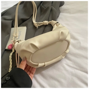 Close-up of beige ruched dumpling bag with heart pendant on soft white bedding